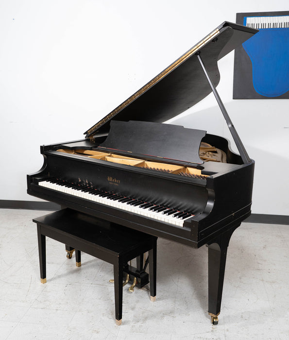 Black grand piano with a bench in a room with a white wall and a blue abstract painting.